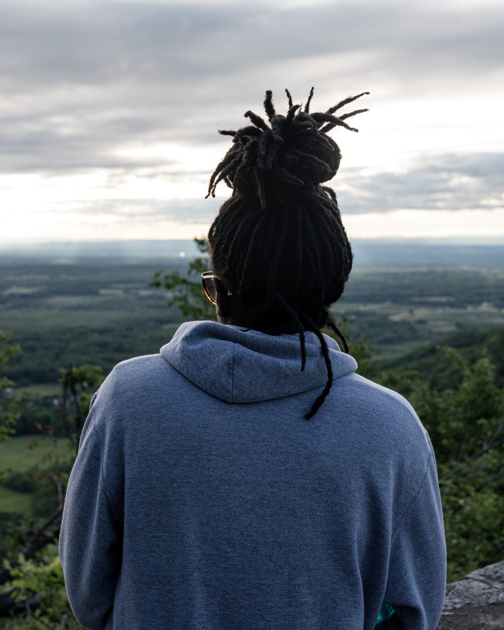 A woman with locs tied up, looking out over green hills