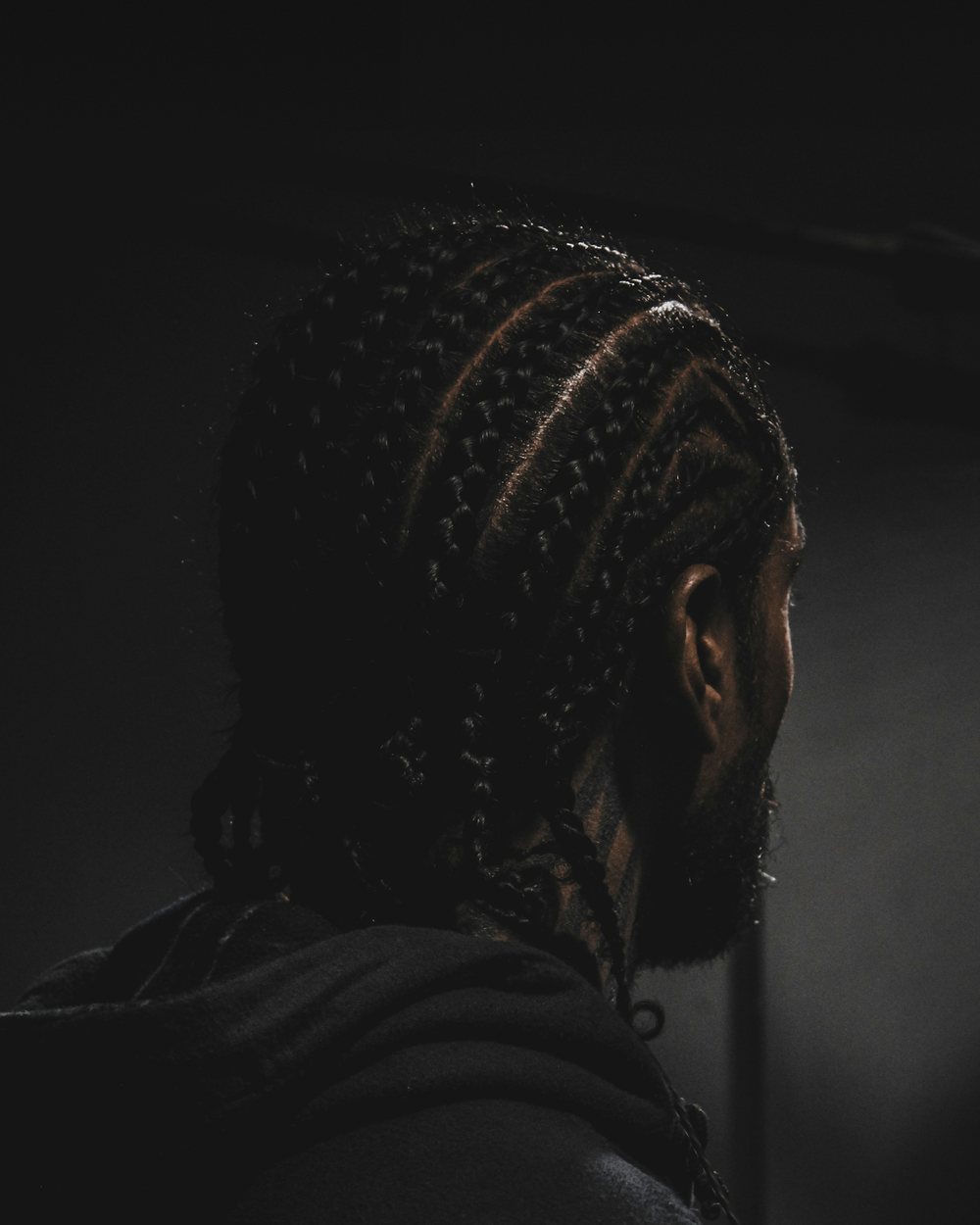 A man with long braids, seen from behind in soft, low light